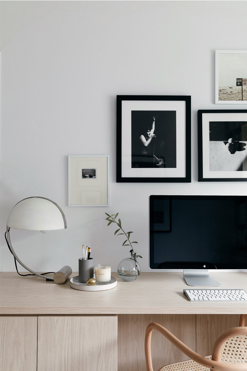 Office with a large computer screen and black and white photos hanging on wall above desk.